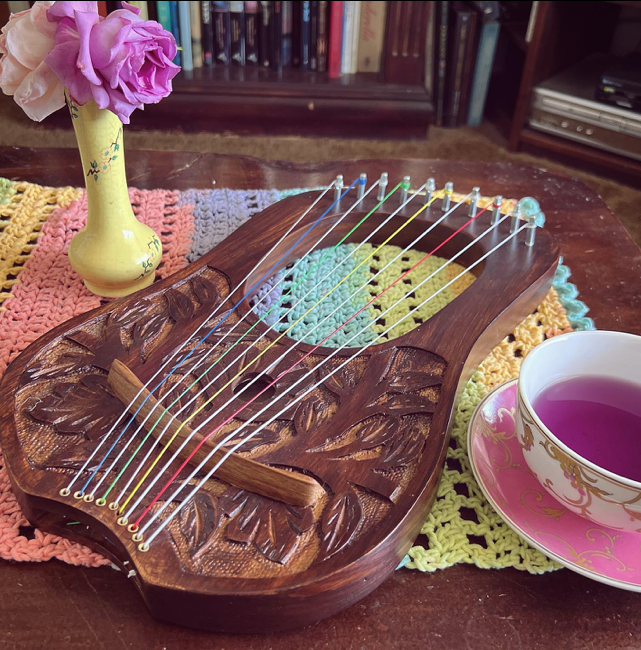 a wooden 10 string lyre lying on a table next to a cup of tea
